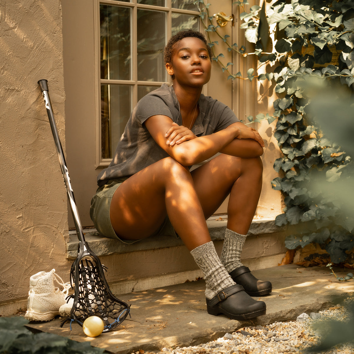 A woman sitting while wearing black backless clogs and casual clothes.