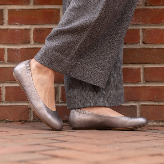 A closeup of metallic silver ballerina flats shown on foot.